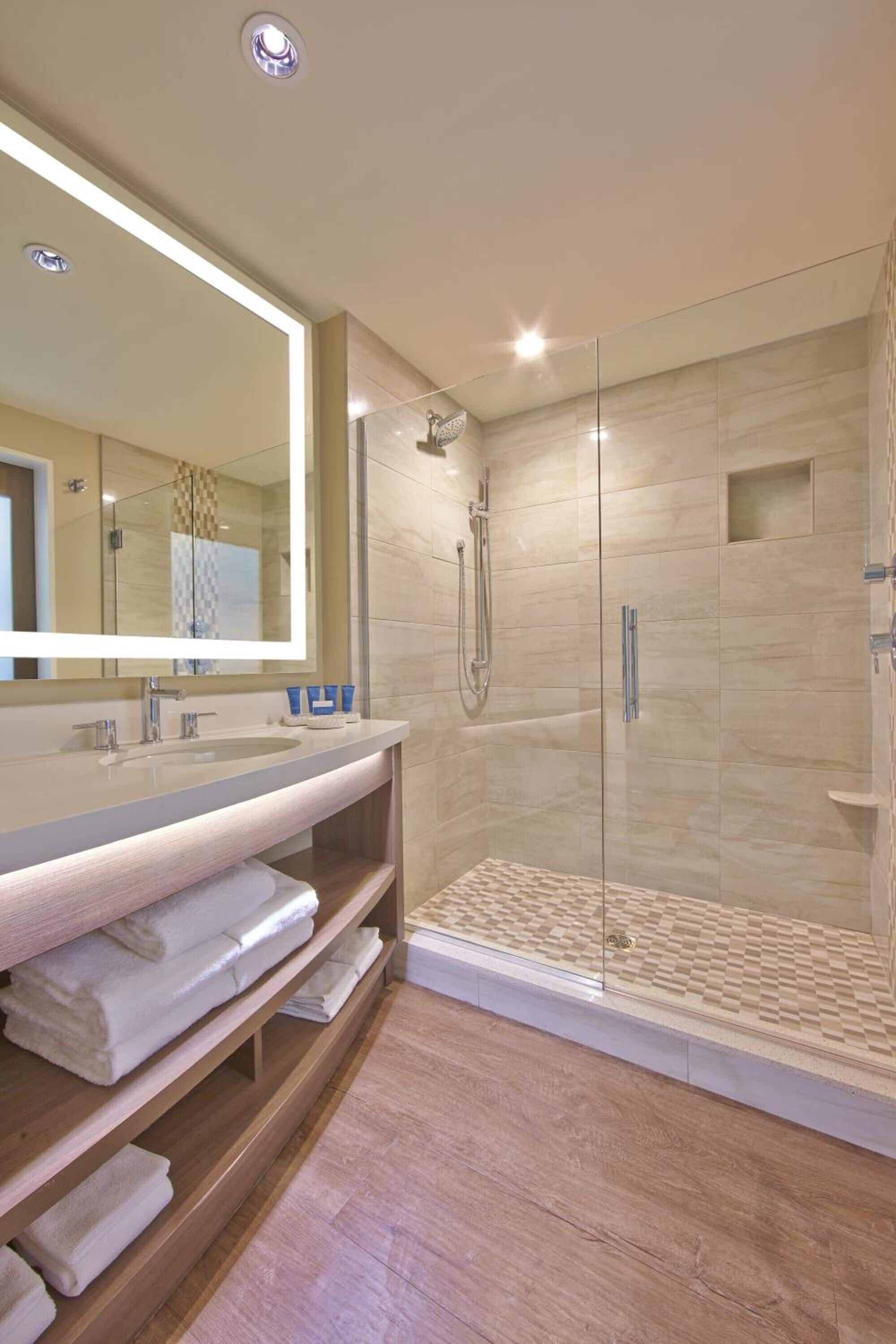 A modern bathroom with a glass-enclosed shower, a large mirror, and a wooden vanity with towels.