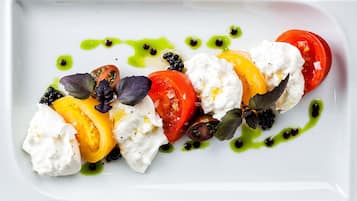 A white plate with a dish of tomatoes, mozzarella, and blackberries, garnished with green sauce.