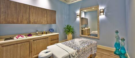 Una habitación con cama, lavamanos, espejo, planta y sillón de masajes.
