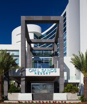 The exterior of Opal Sands Resort with a modern architectural design, featuring a prominent entrance and a clear view of the surrounding palm trees.