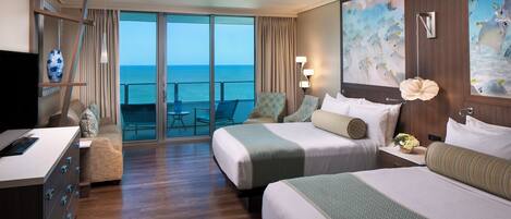 Habitación de hotel con dos camas, un escritorio, un televisor y vistas al mar.