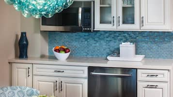 A modern kitchen with white cabinets, a blue tiled backsplash, a stainless steel refrigerator, and a unique blue glass chandelier.
