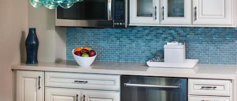 A modern kitchen with white cabinets, a blue tiled backsplash, a stainless steel refrigerator, and a unique blue glass chandelier.