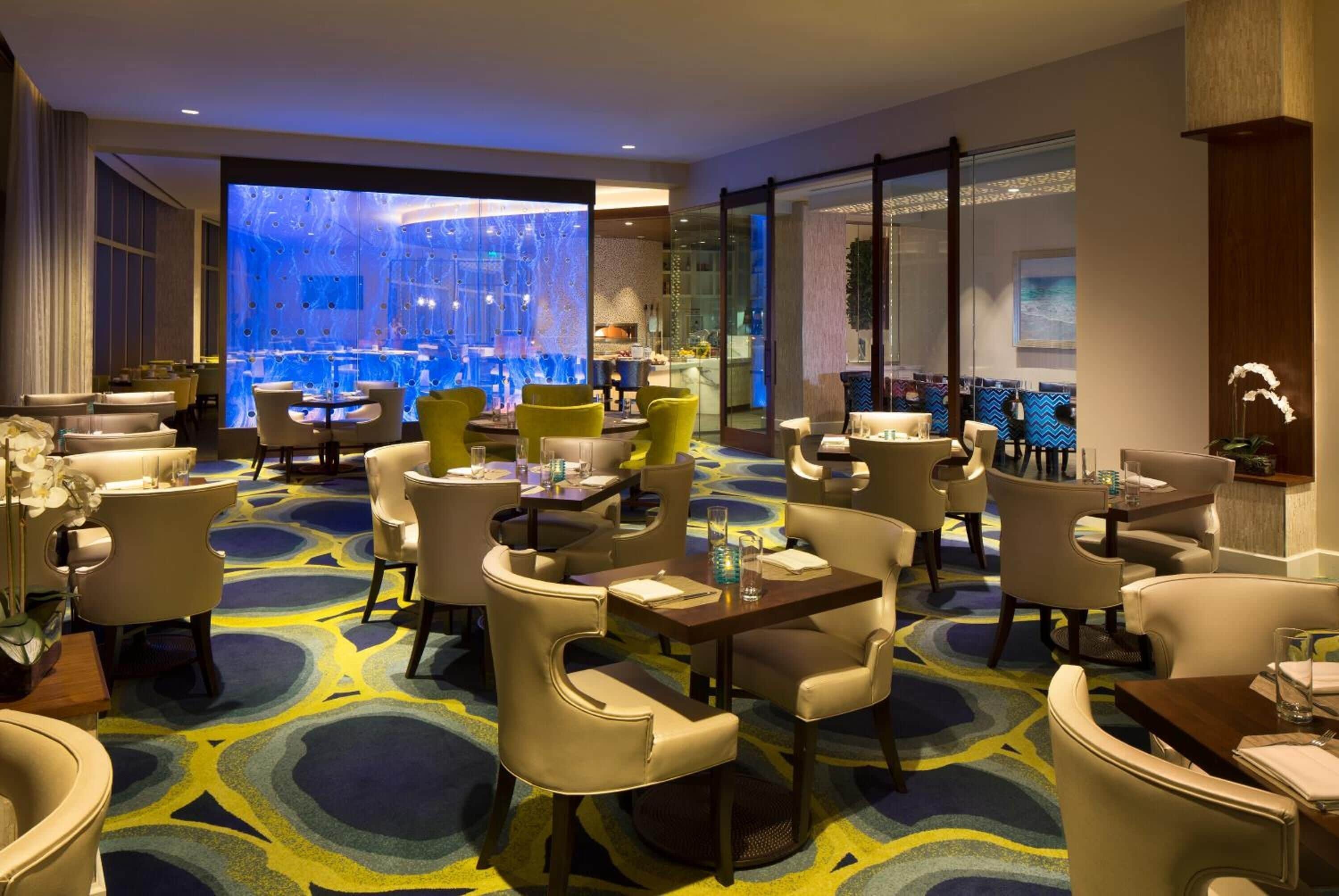 A hotel lobby with multiple seating areas, a large glass wall with a view, and a patterned carpet.