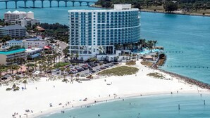Un hotel frente al mar con un edificio grande, una playa y un puente al fondo.