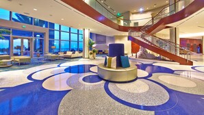A spacious lobby with a central seating area, a staircase, and large windows offering views. - Opal Sands Resort (Clearwater Beach)