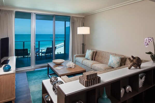 Una habitación de hotel moderna con balcón con vistas al océano, un sofá, una mesa de centro y un televisor.