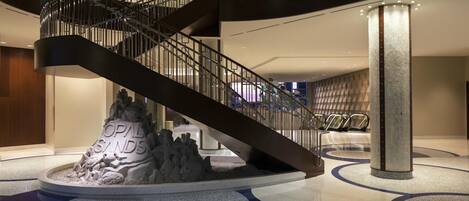 Un moderno vestíbulo de hotel con una escalera de caracol, una escultura central y una zona de estar.