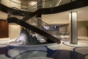 A modern hotel lobby with a spiral staircase, a central sculpture, and a seating area.