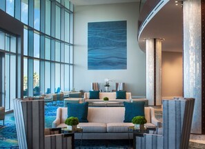 A modern lobby with a large window, a seating area with sofas and chairs, and a large abstract painting on the wall.