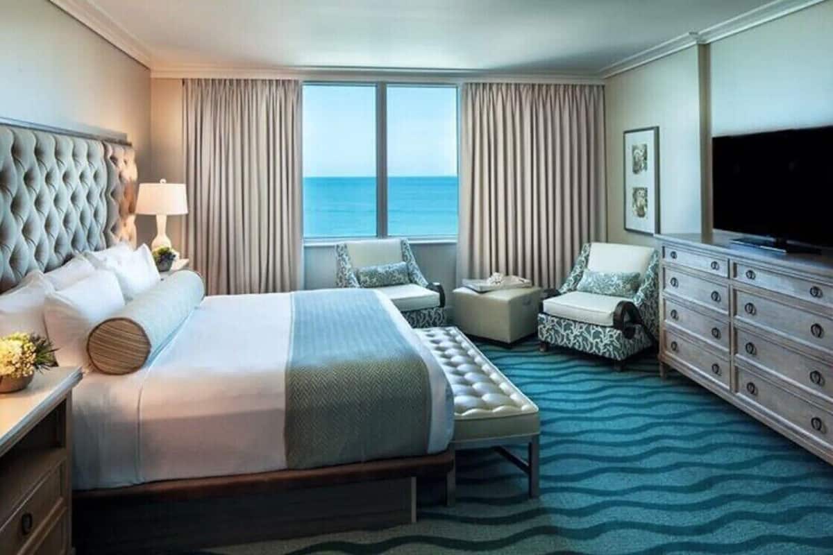 A hotel room with a large bed, a sitting area with a sofa and armchair, a dresser, and a television.