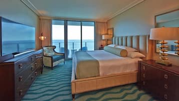 A hotel room with a large bed, a television, a chair, a dresser, and a view of the ocean.