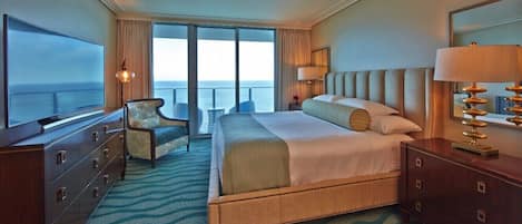 A hotel room with a large bed, a television, a chair, a dresser, and a view of the ocean.