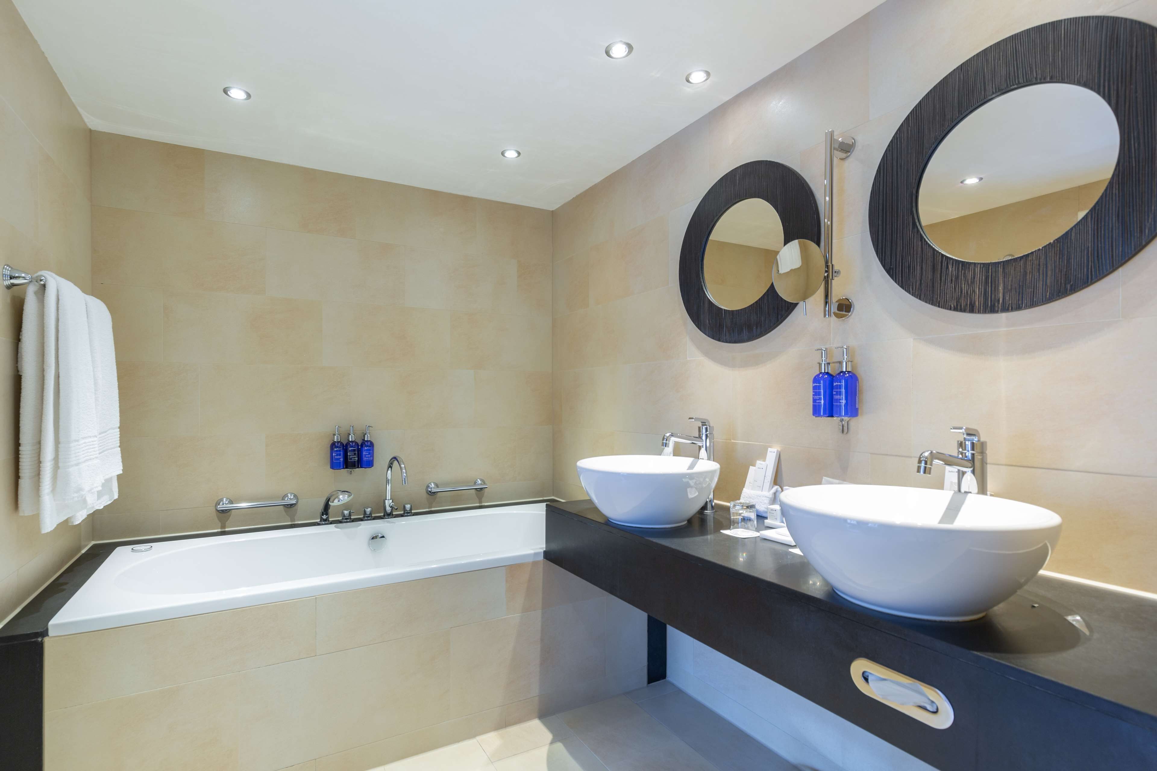 A modern bathroom with two sinks, a large bathtub, and two wall-mounted mirrors.
