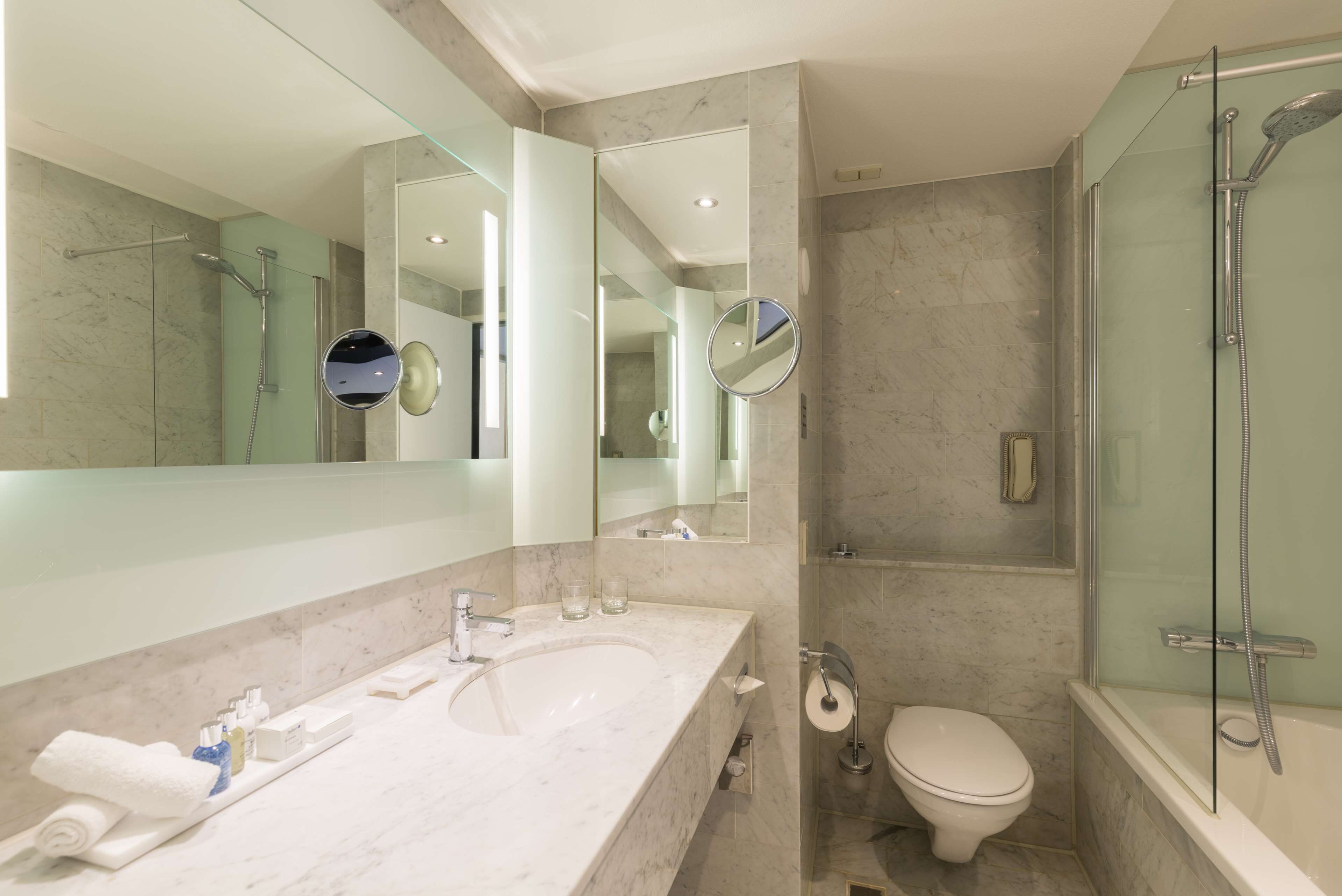 A modern bathroom with a large mirror, a sink, a toilet, and a glass-enclosed shower.