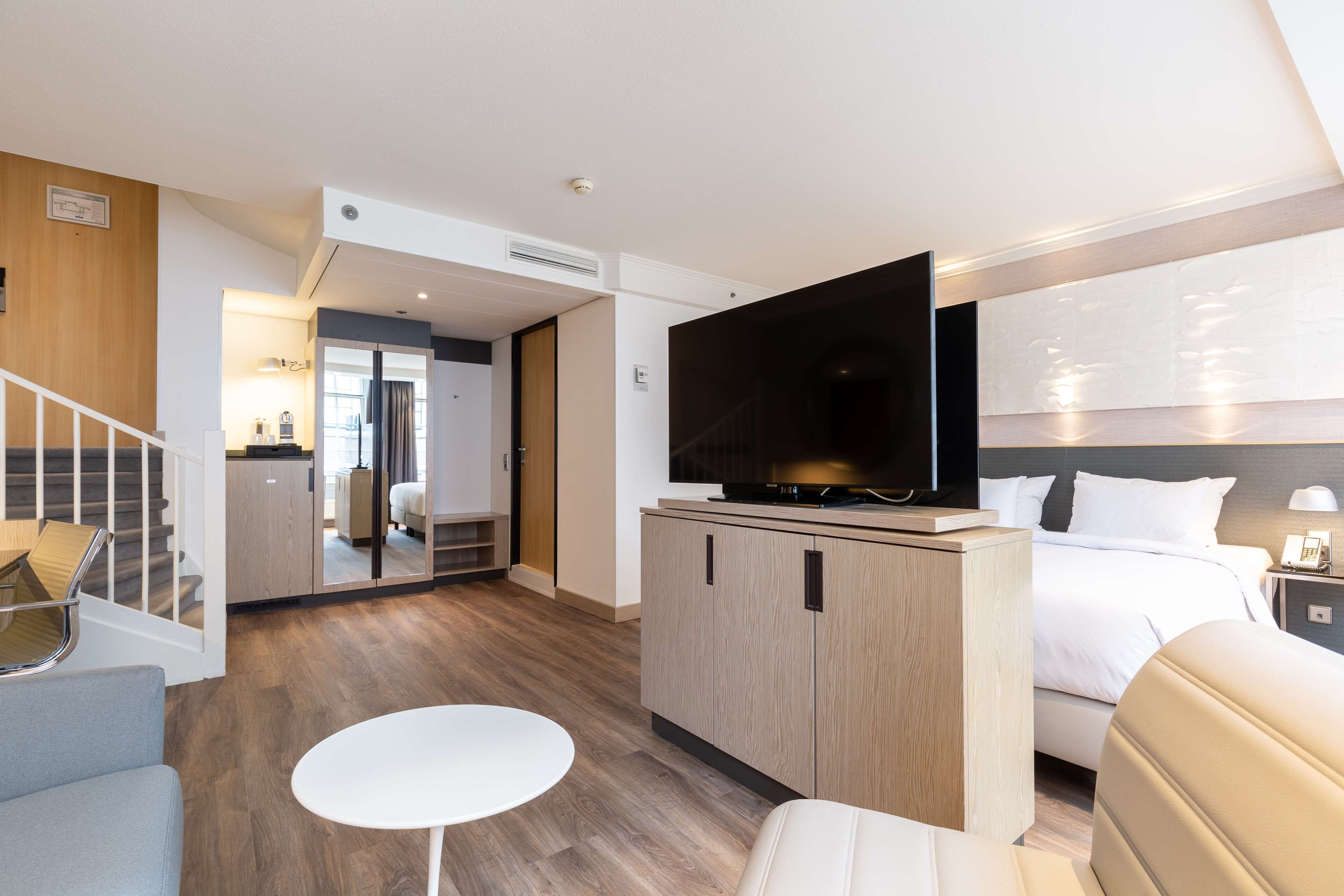 Een moderne hotelkamer met een groot bed, een flatscreen-televisie, een klein rond tafeltje en een zithoek met een stoel.