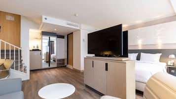Een moderne hotelkamer met een groot bed, een flatscreen-televisie, een klein rond tafeltje en een zithoek met een stoel.