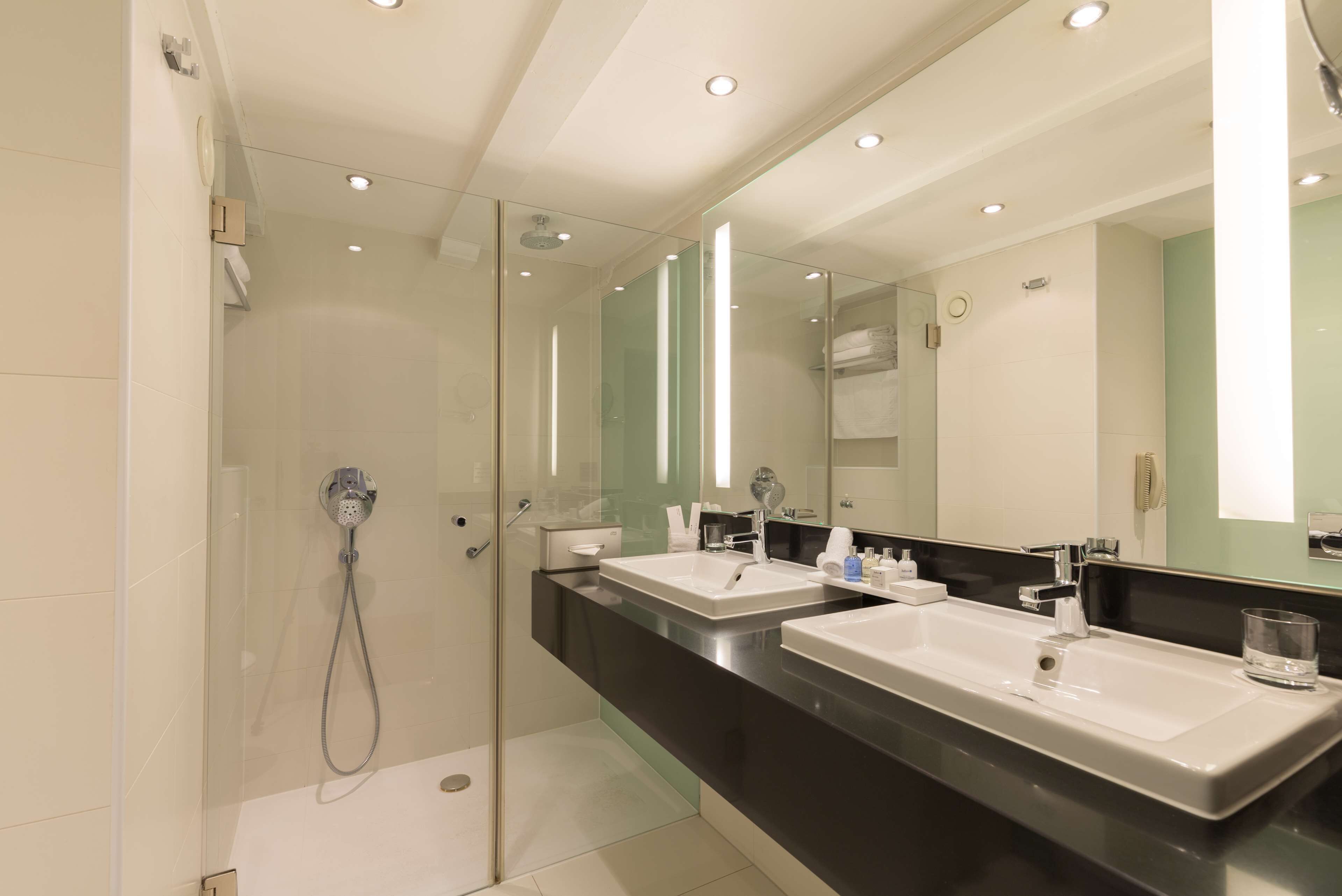 Une salle de bain moderne avec deux lavabos, une douche à l’italienne en verre et un grand miroir.