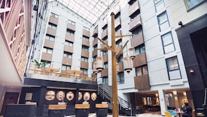 Eine moderne Hotelhalle mit einer zentralen Holzskulptur, verschiedenen Sitzbereichen und einer hohen Decke mit Oberlicht.