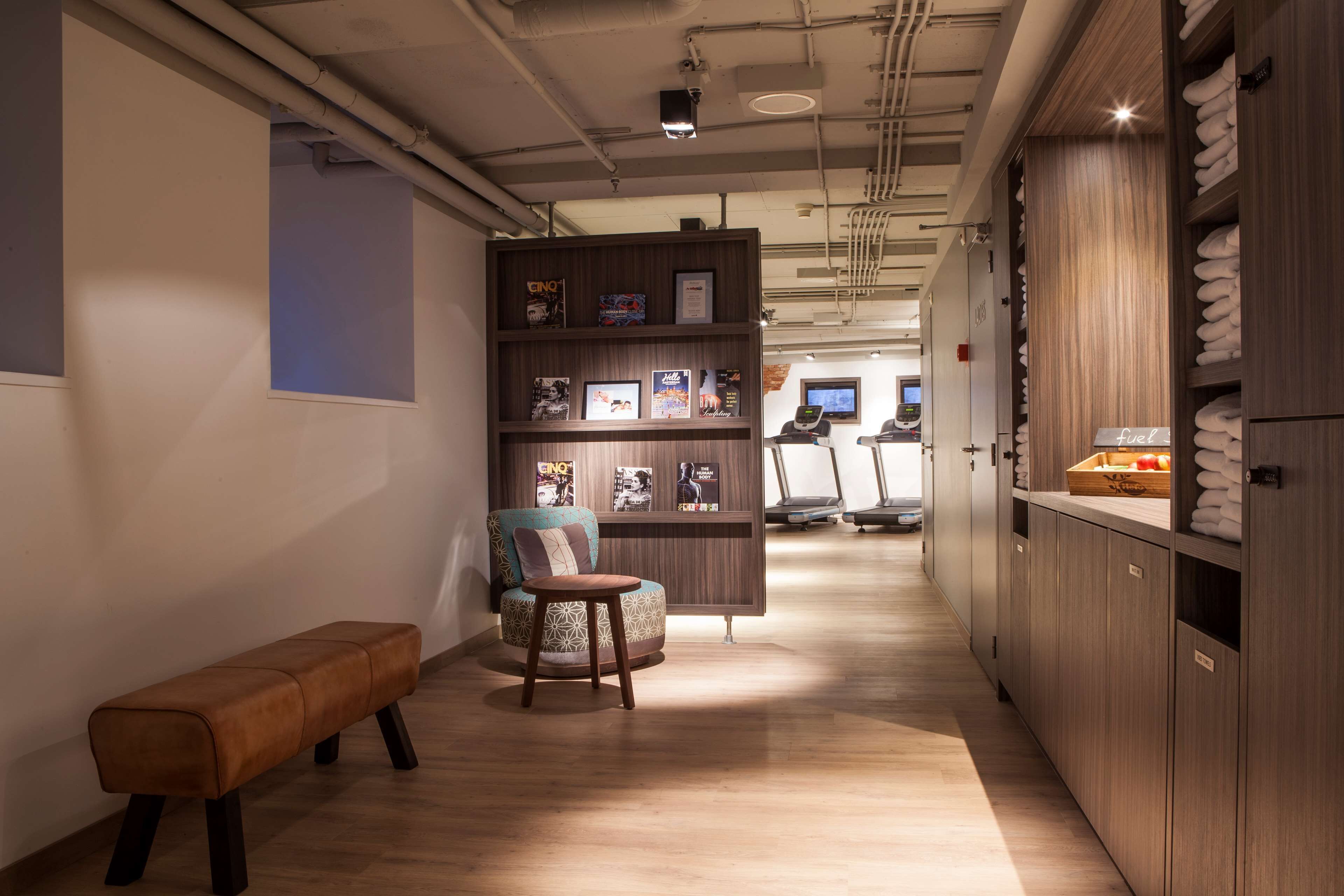 Un pasillo con un banco de madera, un área de descanso, una exposición de cuadros enmarcados y un mostrador con toallas.