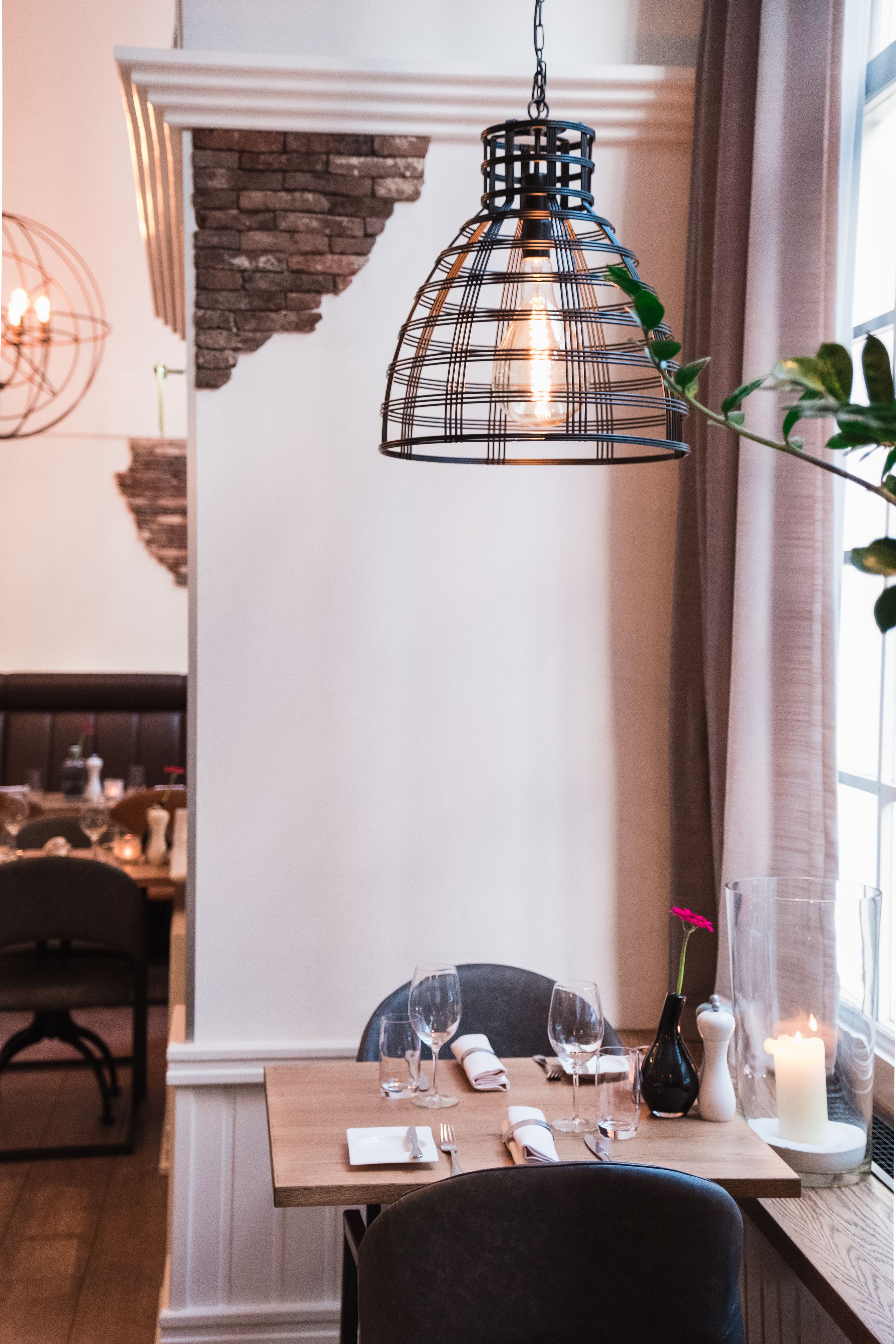 Een eettafel gedekt met een kaars, een vaas met een bloem en een zwart hanglamp.