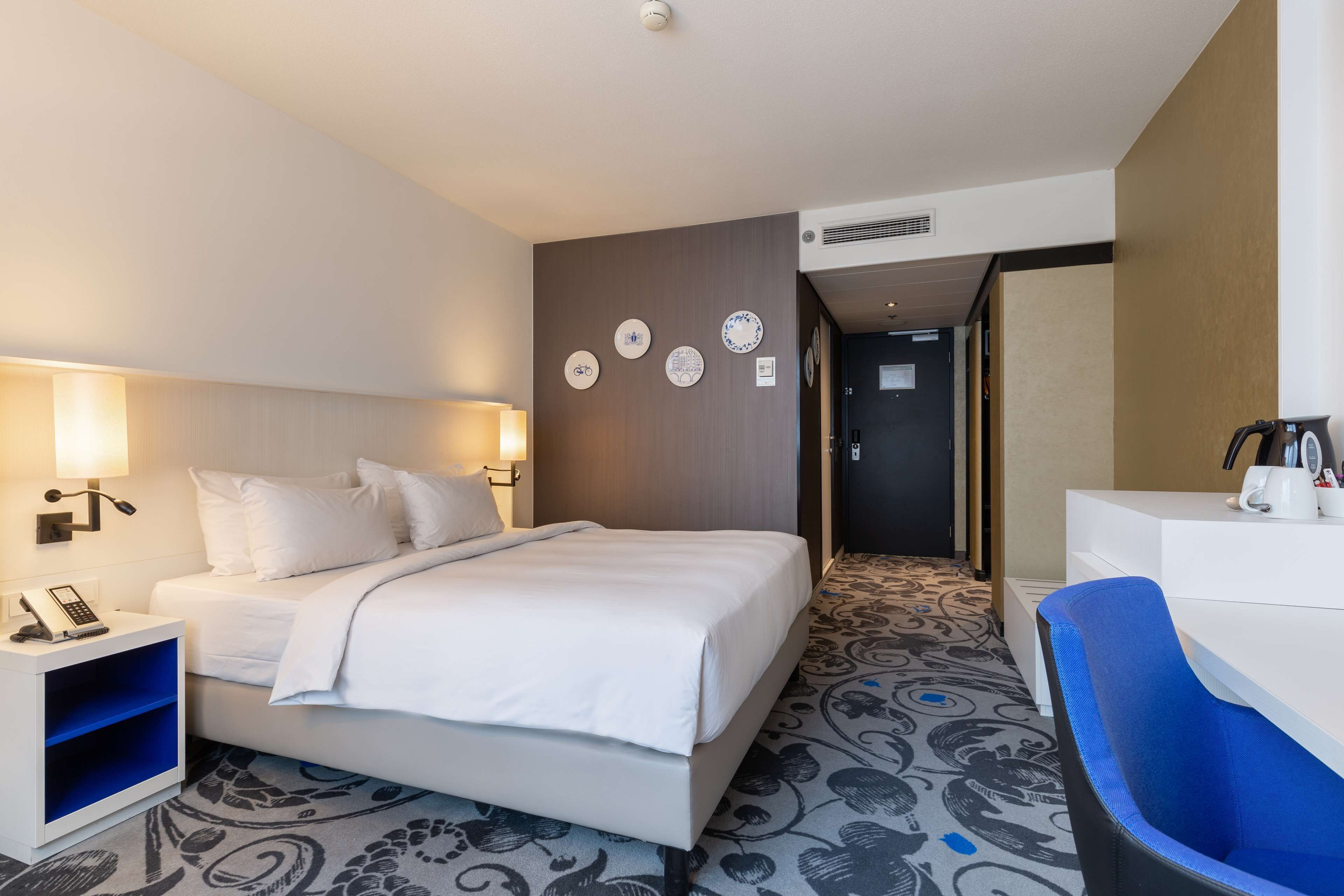 Una habitación de hotel con cama, mesita de noche, lámpara y escritorio con silla.