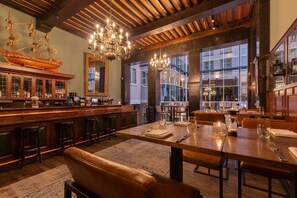 A bar area with wooden bar stools, a ship model, and a chandelier. Tables are set with tableware. - Radisson Blu Hotel, Amsterdam City Center (Amsterdam)