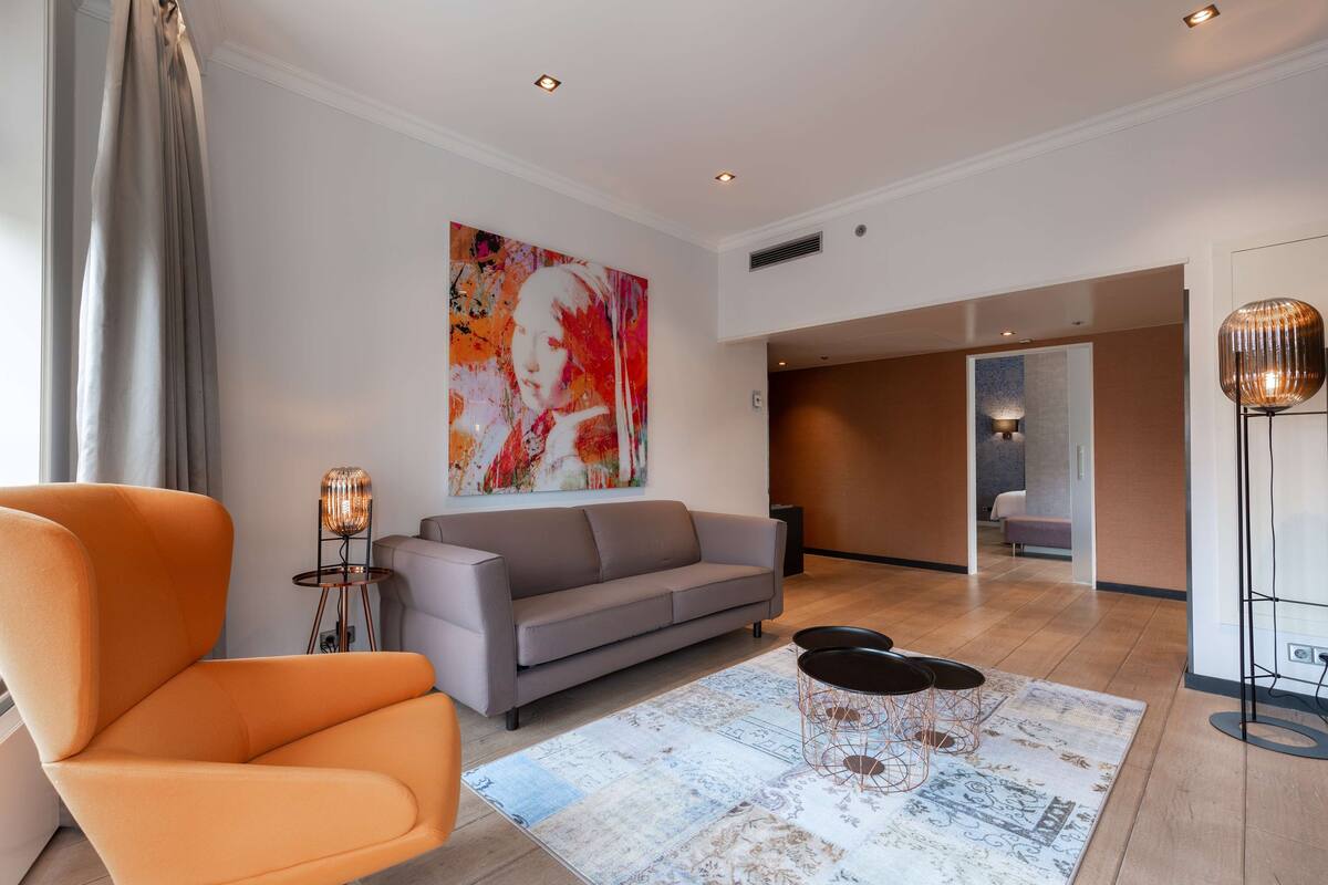 A modern living room with a grey sofa, an orange armchair, and a large abstract painting on the wall.