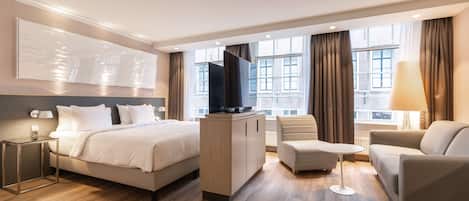 A modern hotel room with a bed, a desk, a TV, a sofa, and a lamp.