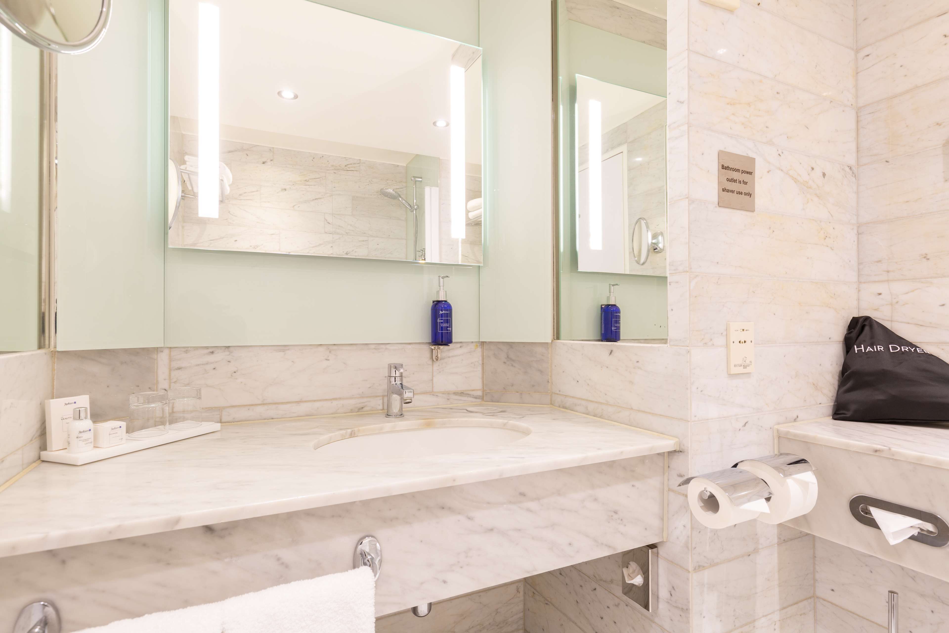Baño con lavamanos de mármol, un espejo grande, un perchero y un letrero que indica que es solo para duchas.