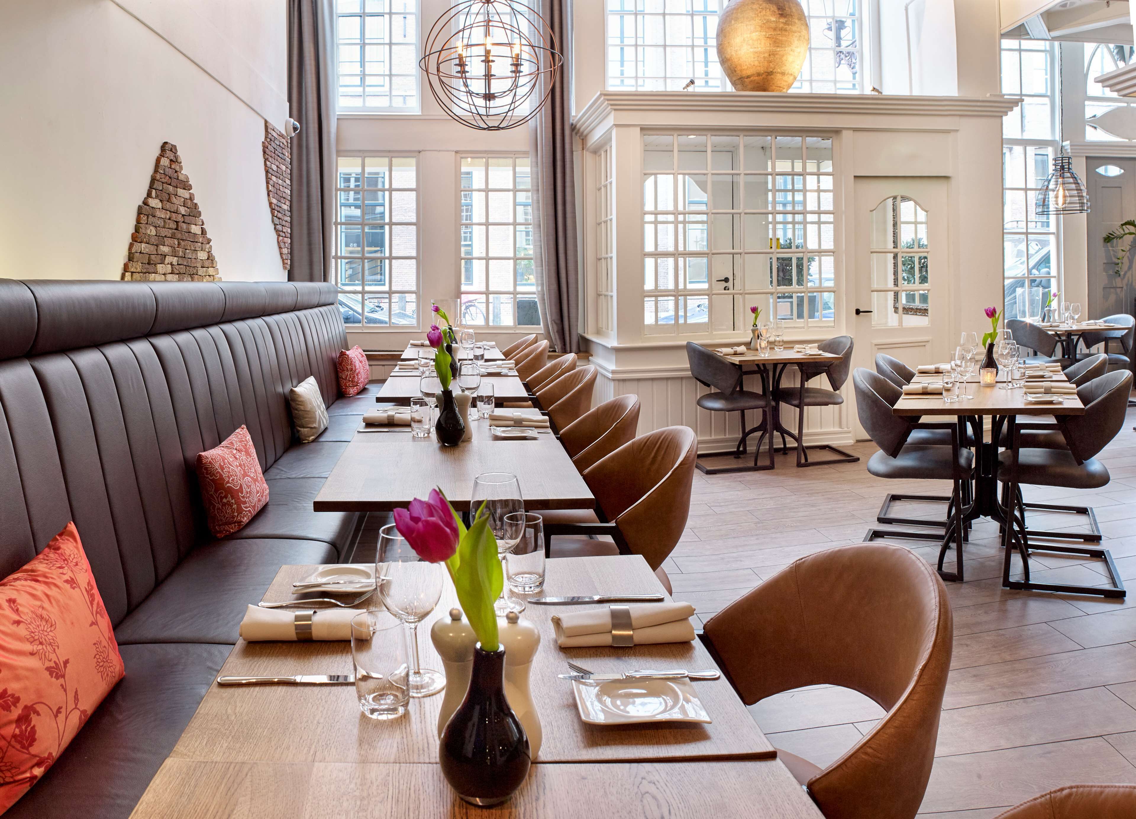 Un restaurante con una larga mesa de comedor, asientos acolchados y ventanas amplias.
