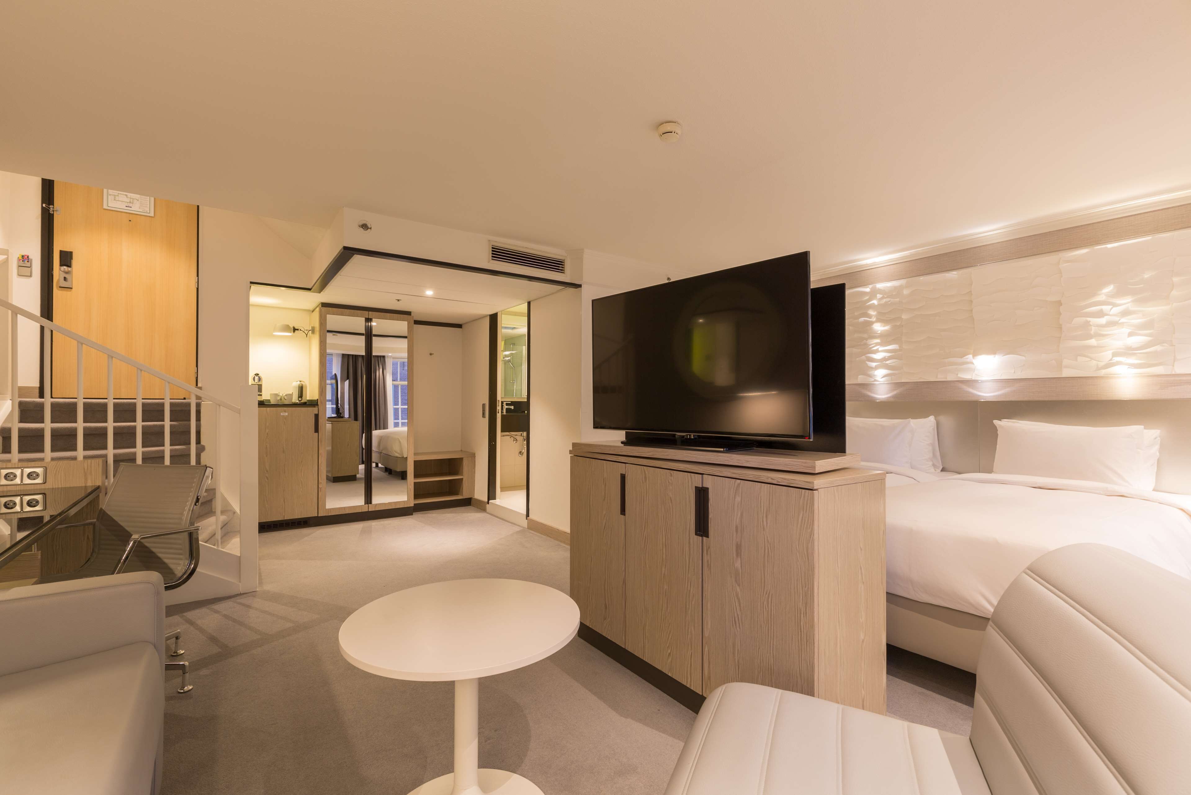 A hotel room with a bed, a TV, a small table, and a staircase leading to a bathroom.