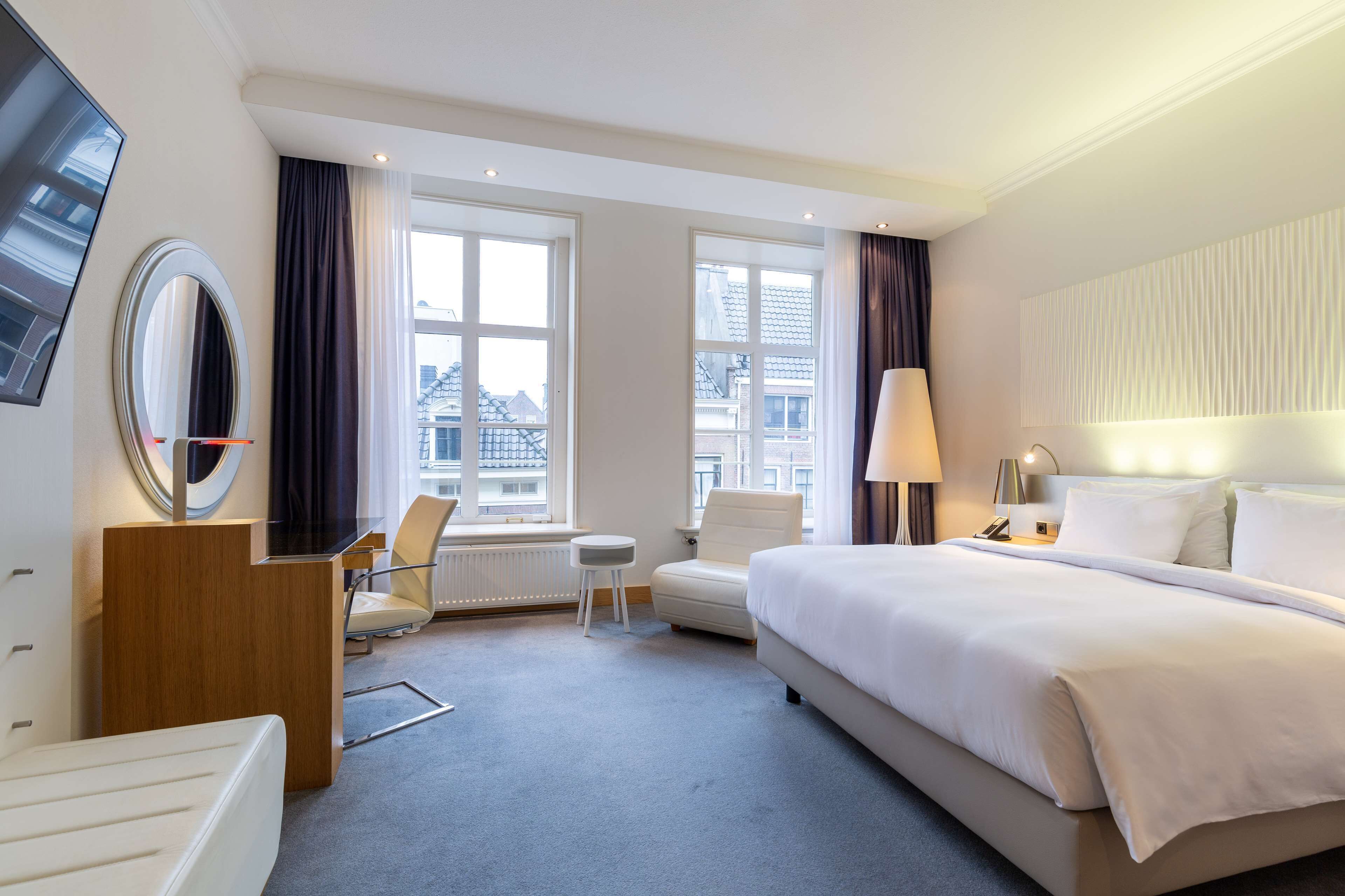 A hotel room with a large bed, a desk, a chair, a small table, and a TV mounted on the wall.