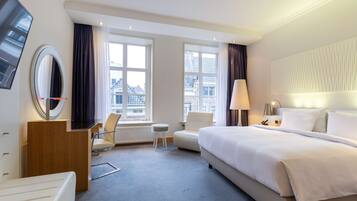 A hotel room with a large bed, a desk, a chair, a small table, and a TV mounted on the wall.