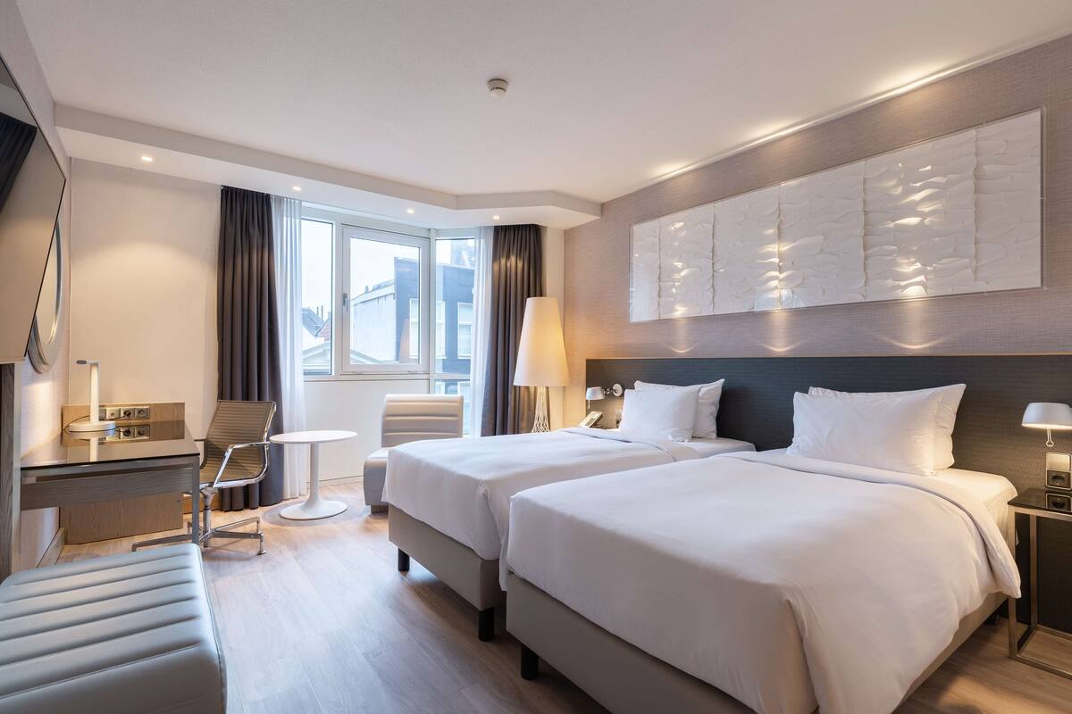 A hotel room with two beds, a desk, a chair, and a small table.