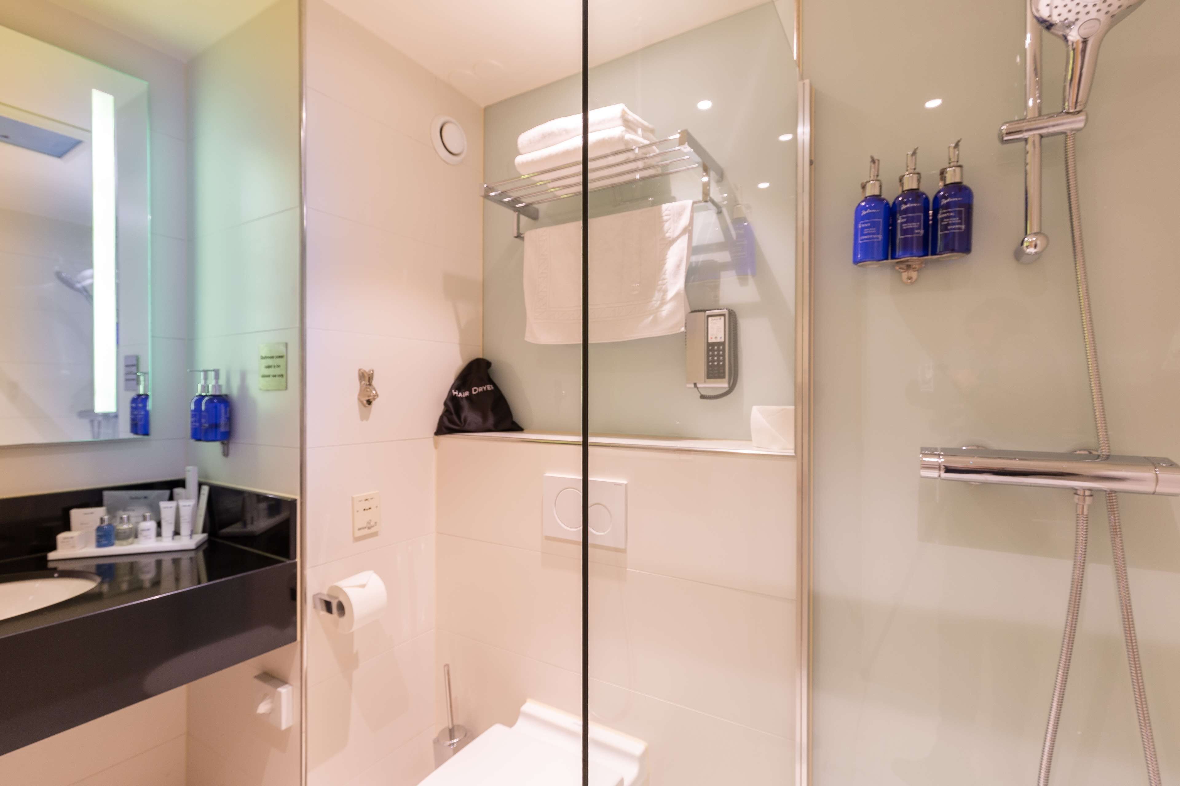 Un baño moderno con cabina de ducha de vidrio, un bolso de cuero negro sobre el mostrador y artículos de tocador en el lavabo.