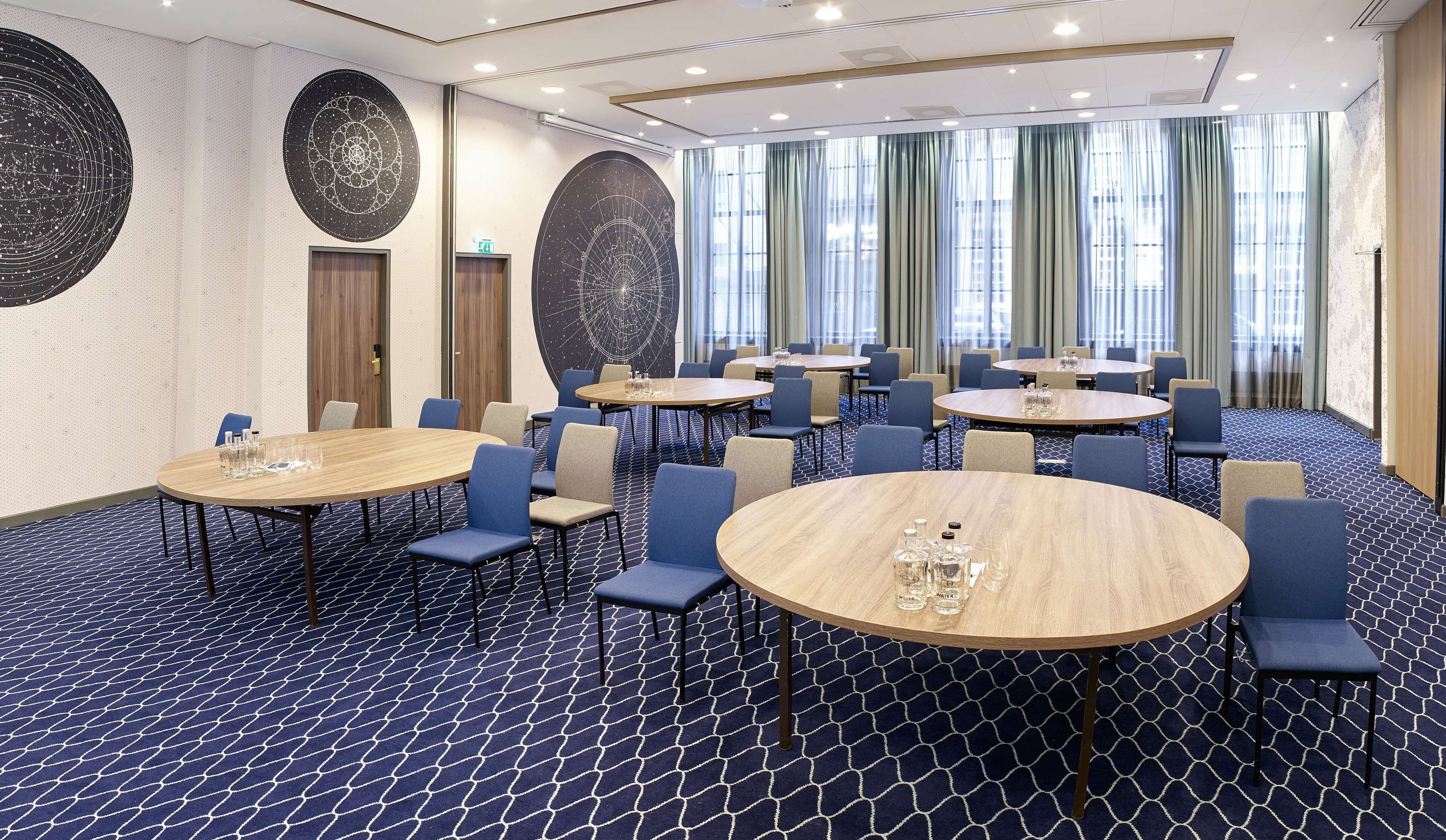 Un salón de conferencias de hotel con varias mesas redondas, sillas azules y una alfombra estampada.