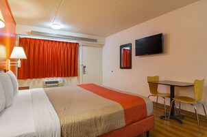 Habitación de hotel con cama, una mesa y dos sillas, televisor y ventana con cortinas.