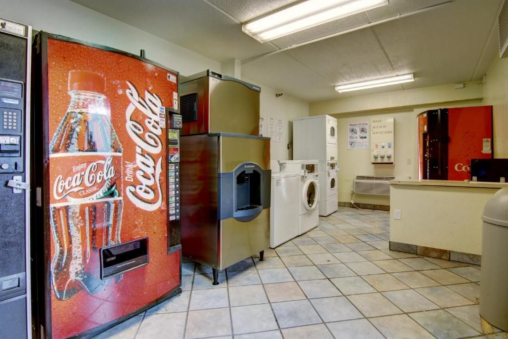 A laundromat with a Coca-Cola vending machine, washers, dryers, and a trash can.