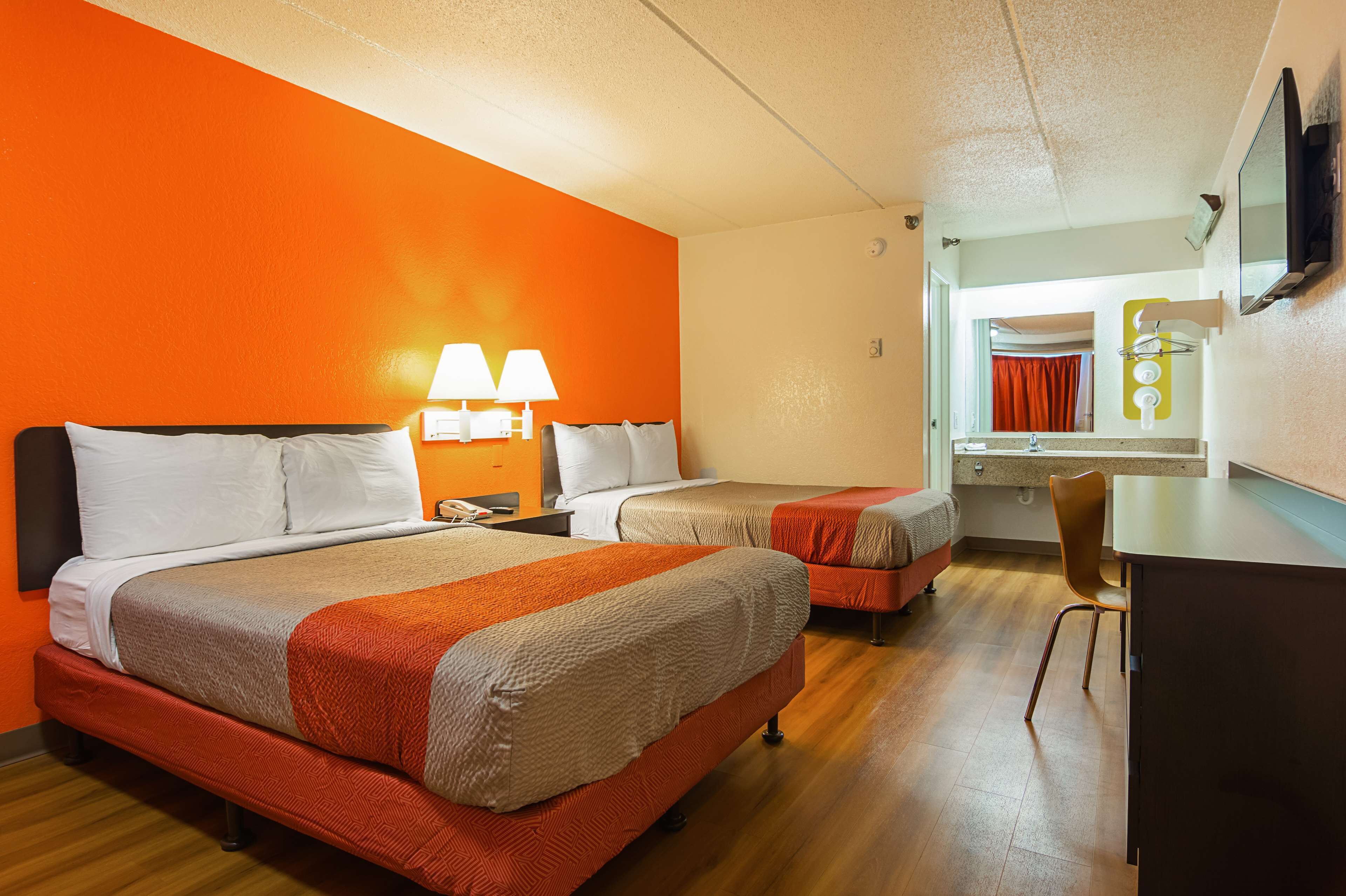 A hotel room with two beds, a desk, a chair, and a TV.