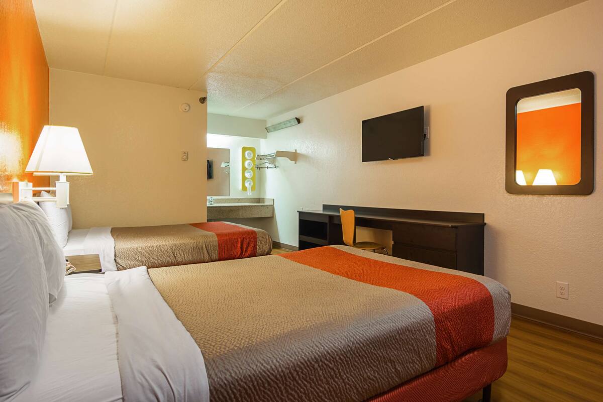 Une chambre d’hôtel avec deux lits, un bureau, une télévision et une salle de bain visible au fond.