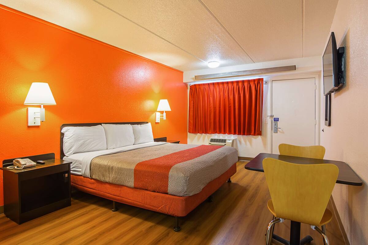 Une chambre d’hôtel comprenant un lit, des lampes de chevet, une table avec une chaise et un téléviseur fixé au mur.