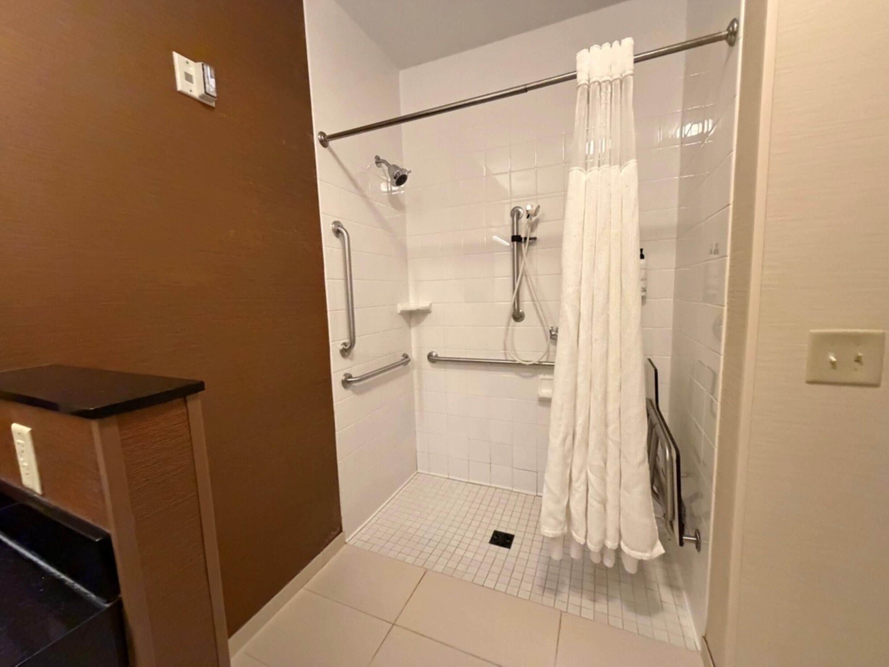 A bathroom with white tiled walls, a shower with a glass door, and a white towel hanging on a metal bar.