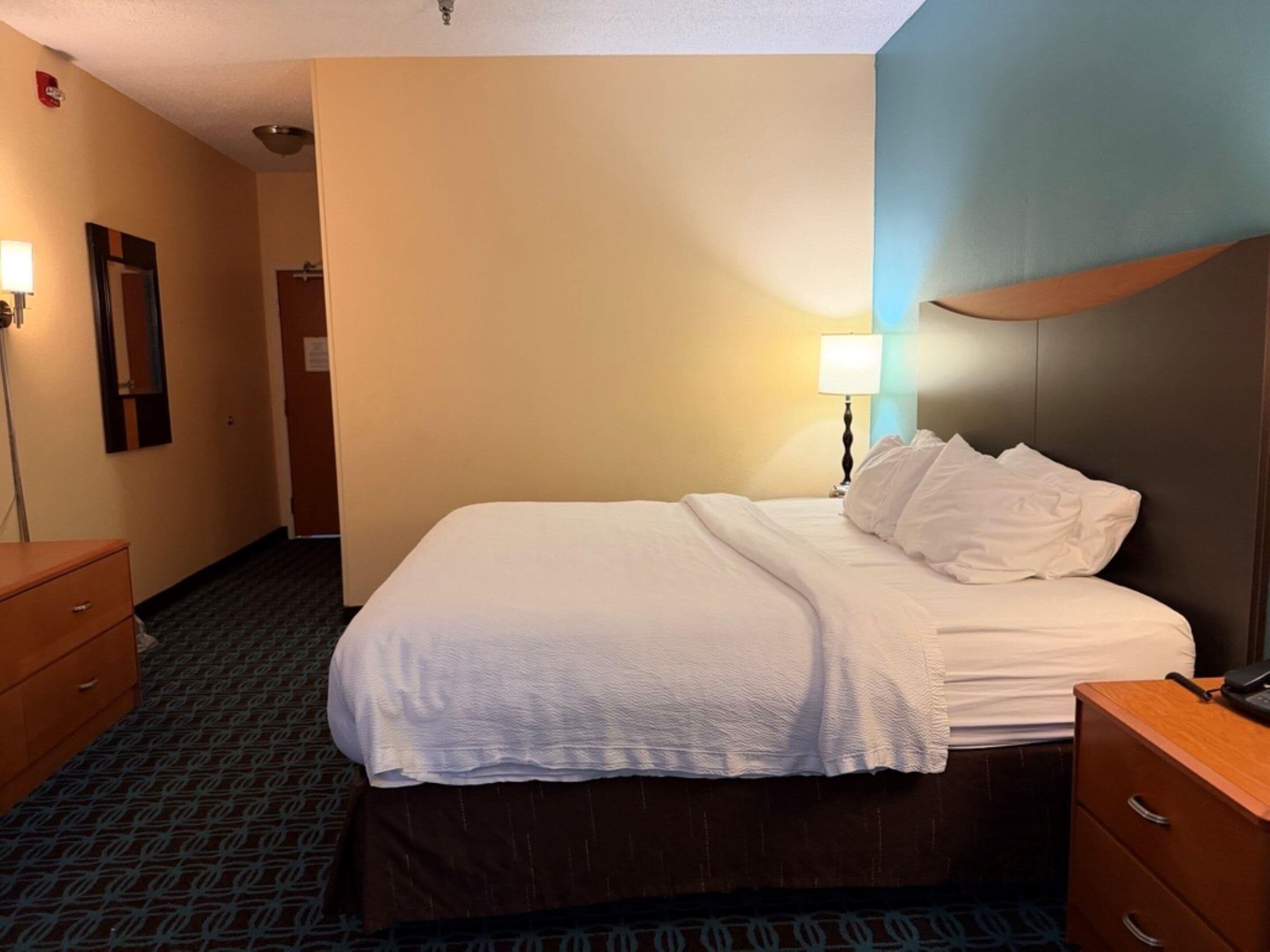 A hotel room with a bed, a nightstand, a lamp, a dresser, and a mirror.
