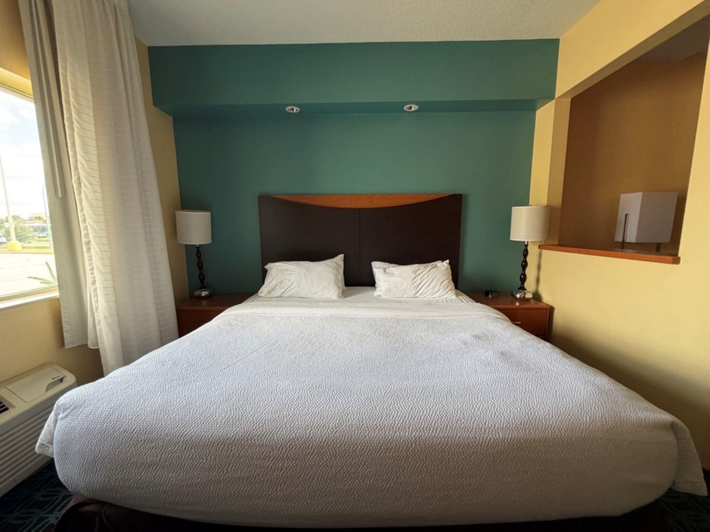 A hotel room with a large bed, two bedside tables, and a window with curtains.
