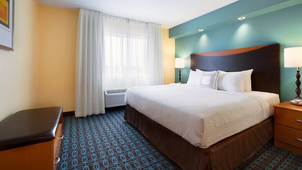 A hotel room with a large bed, a bedside table, a lamp, and a window with curtains. - SureStay by Best Western Bismarck (Bismarck)