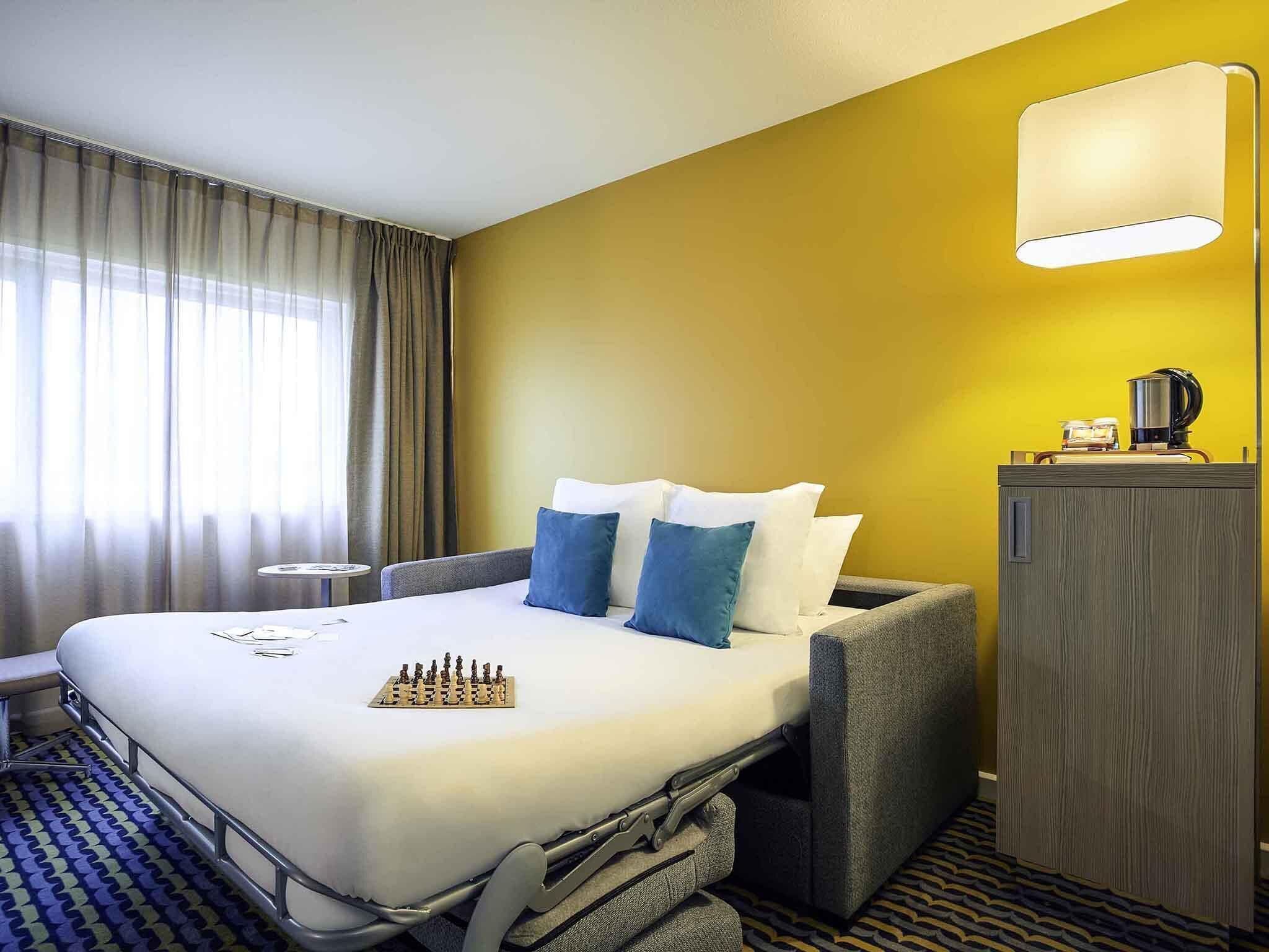 Una camera d'albergo con un letto, un comodino, una lampada e un minibar.