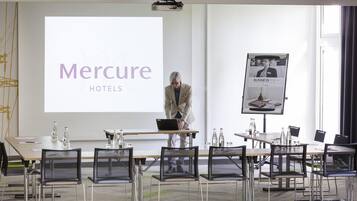 A conference room with a presentation screen displaying 'Mercure HOTELS,' a projector, and a poster on the wall.
