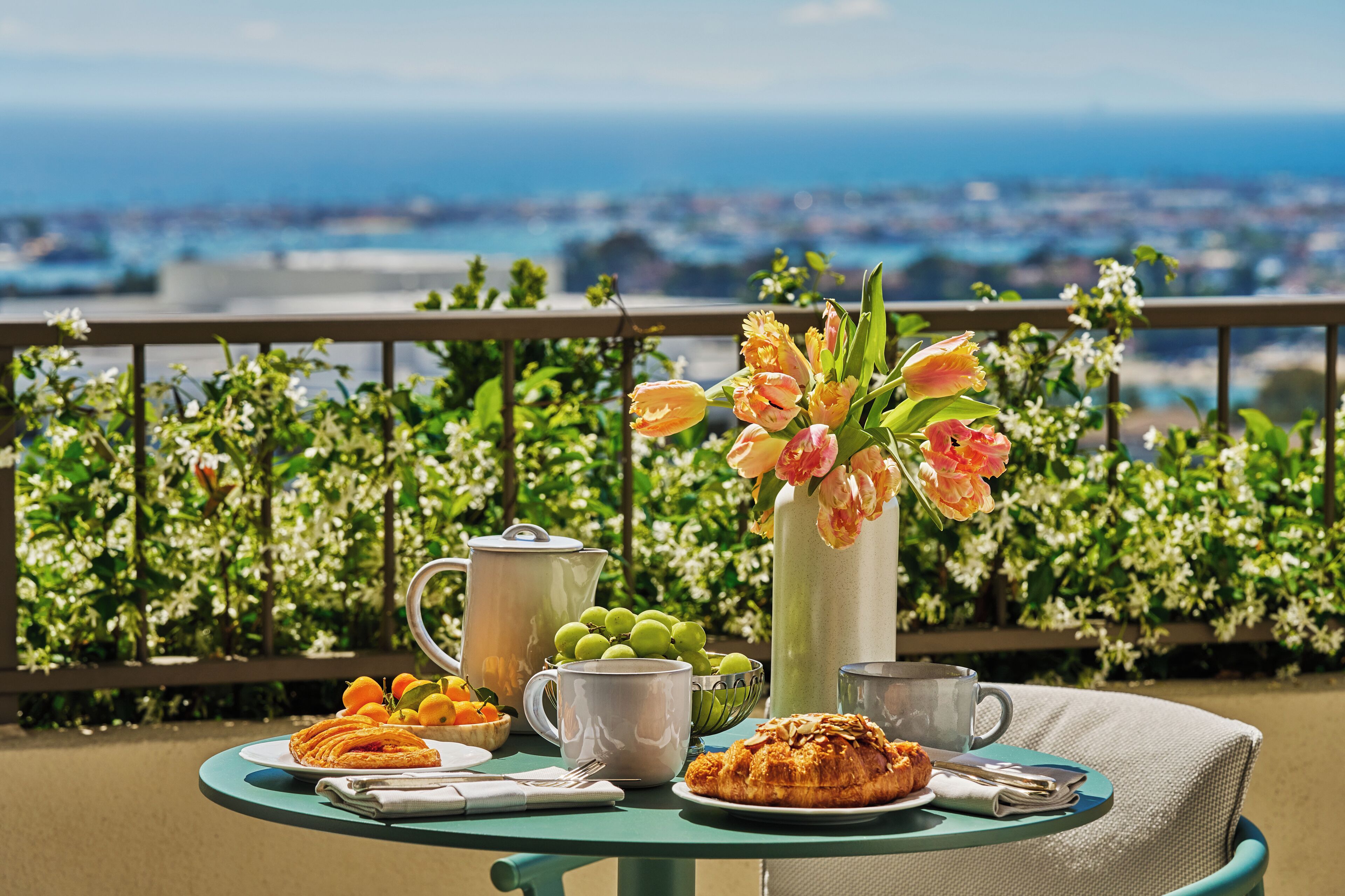 A table with breakfast items, a pitcher of flowers, and a view of the city.