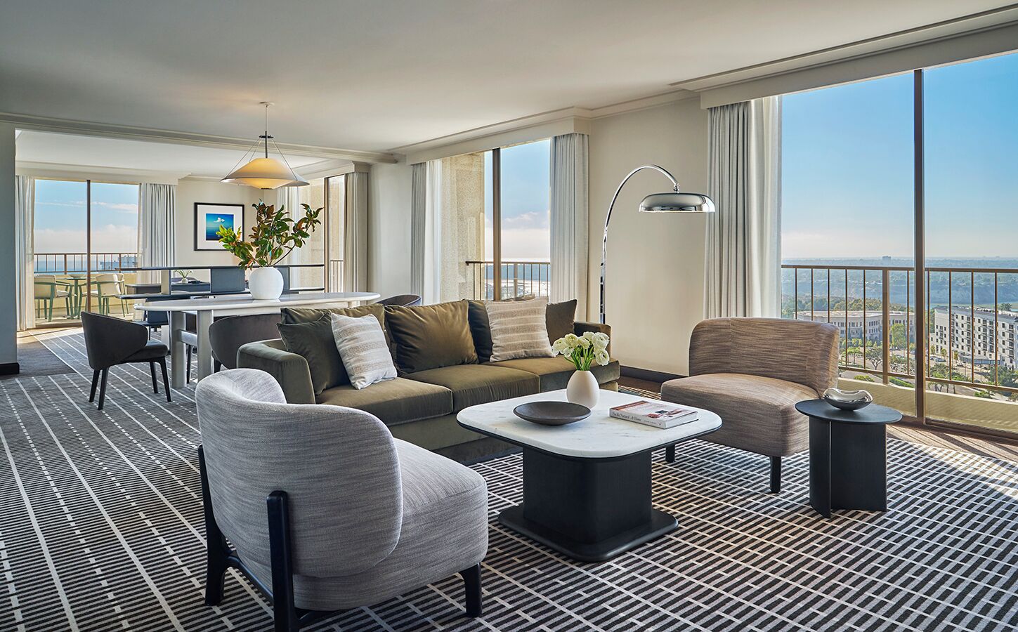 A modern hotel room with a balcony, a sofa, a coffee table, and a dining area.